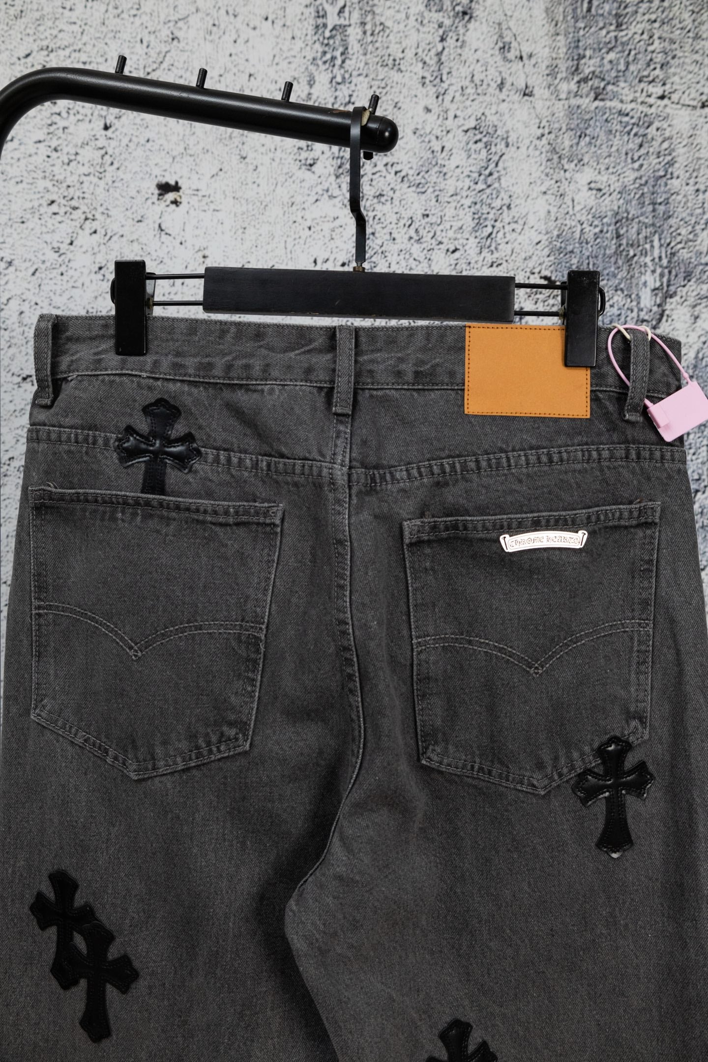 Dark gray denim pants with pockets, black cross appliques, and orange tag