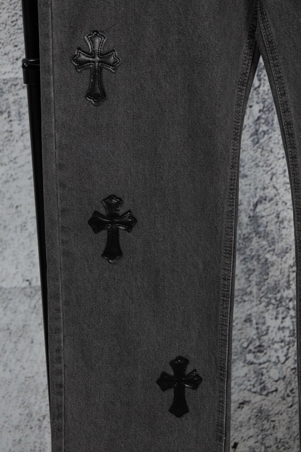 Dark denim pants with multiple black cross embroideries on the leg