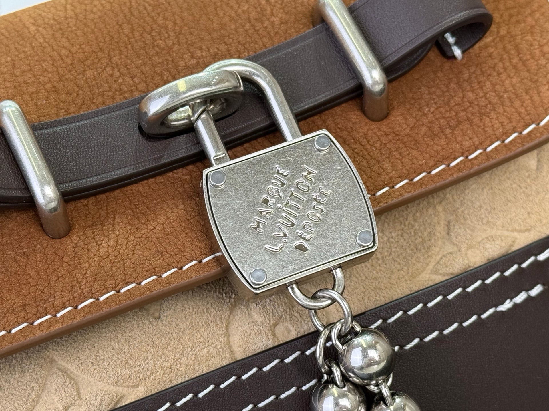 Brown and tan backpack clasp hardware with engraved metal lock and stitched trim