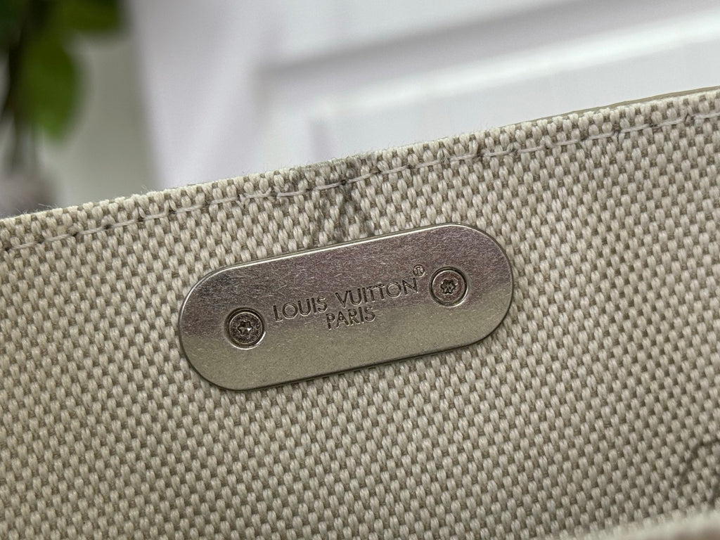 Rectangular metal logo plaque reading Louis Vuitton Paris on tan textured fabric