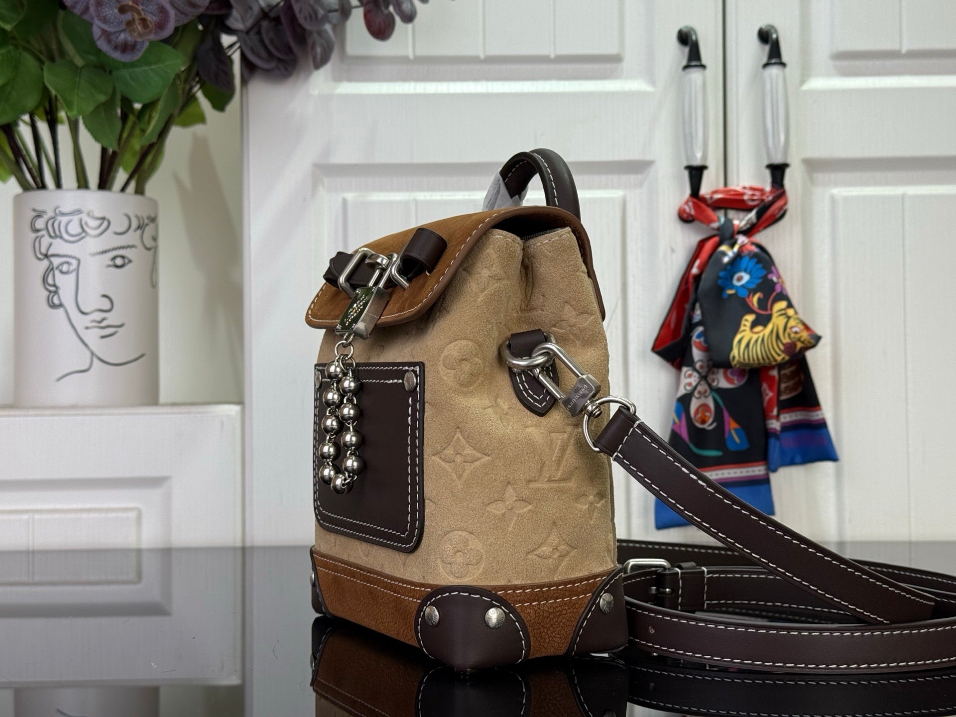 Tan and brown mini backpack with top handle, patterned front panel, and chain detail