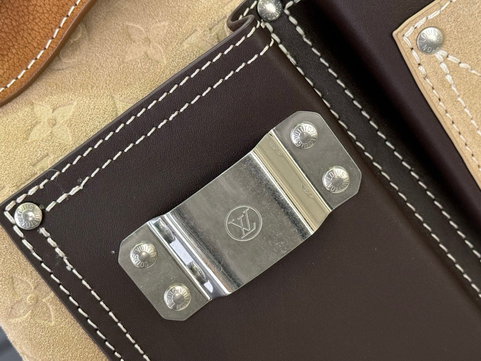 Louis Vuitton metal clasp on dark leather flap with white contrast stitching, tan trim.