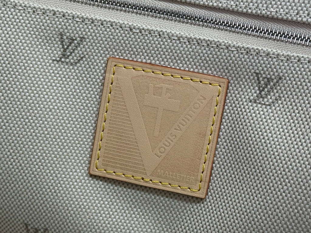 Louis Vuitton logo label patch stitched on gray canvas, tan border.