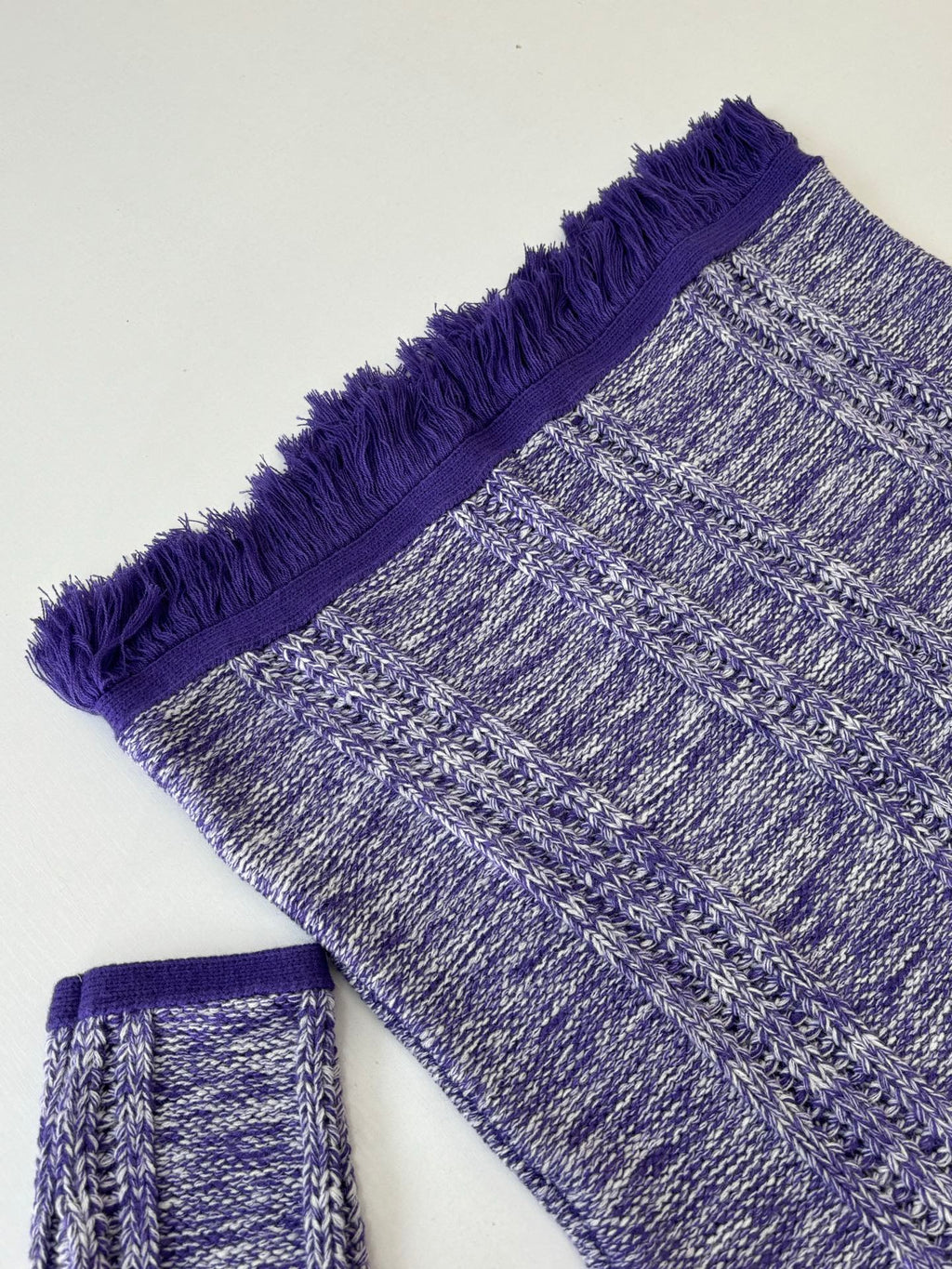 Knit sweater sleeve and hem with heathered blue texture and purple fringe trim