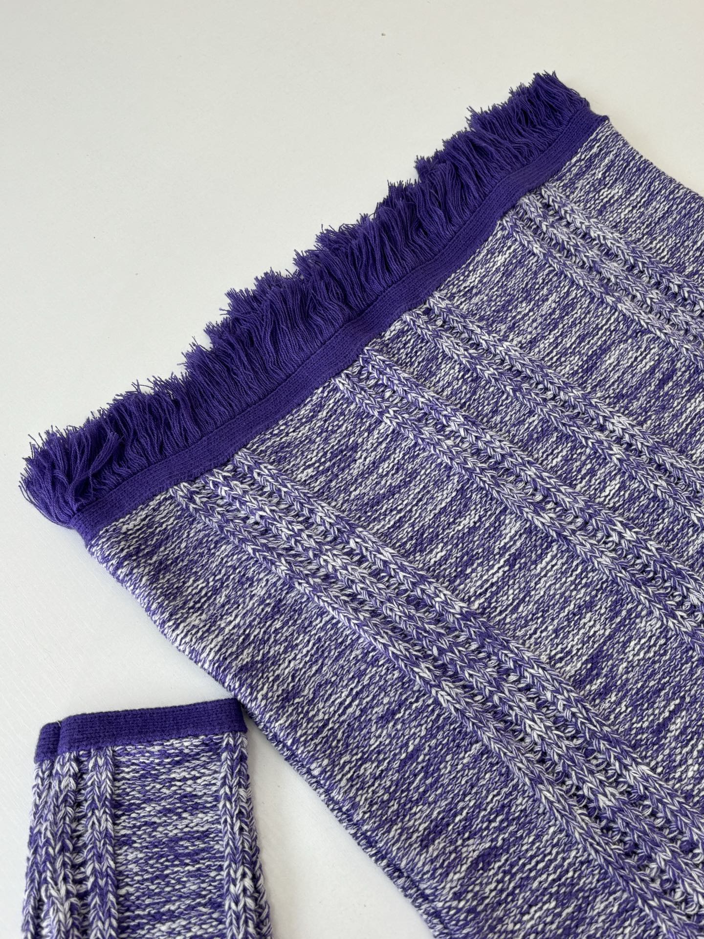 Knit sweater sleeve and hem with heathered blue texture and purple fringe trim