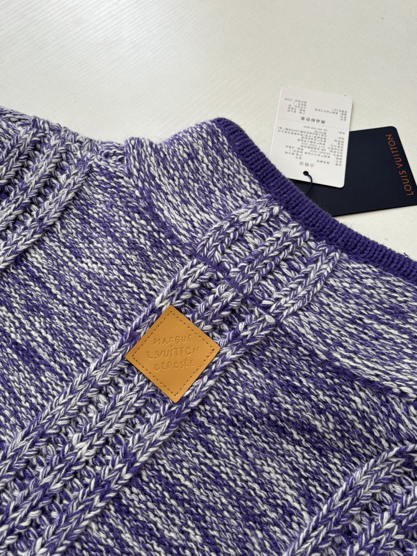 Knit sweater chest close-up with stitched logo patch and heathered blue pattern