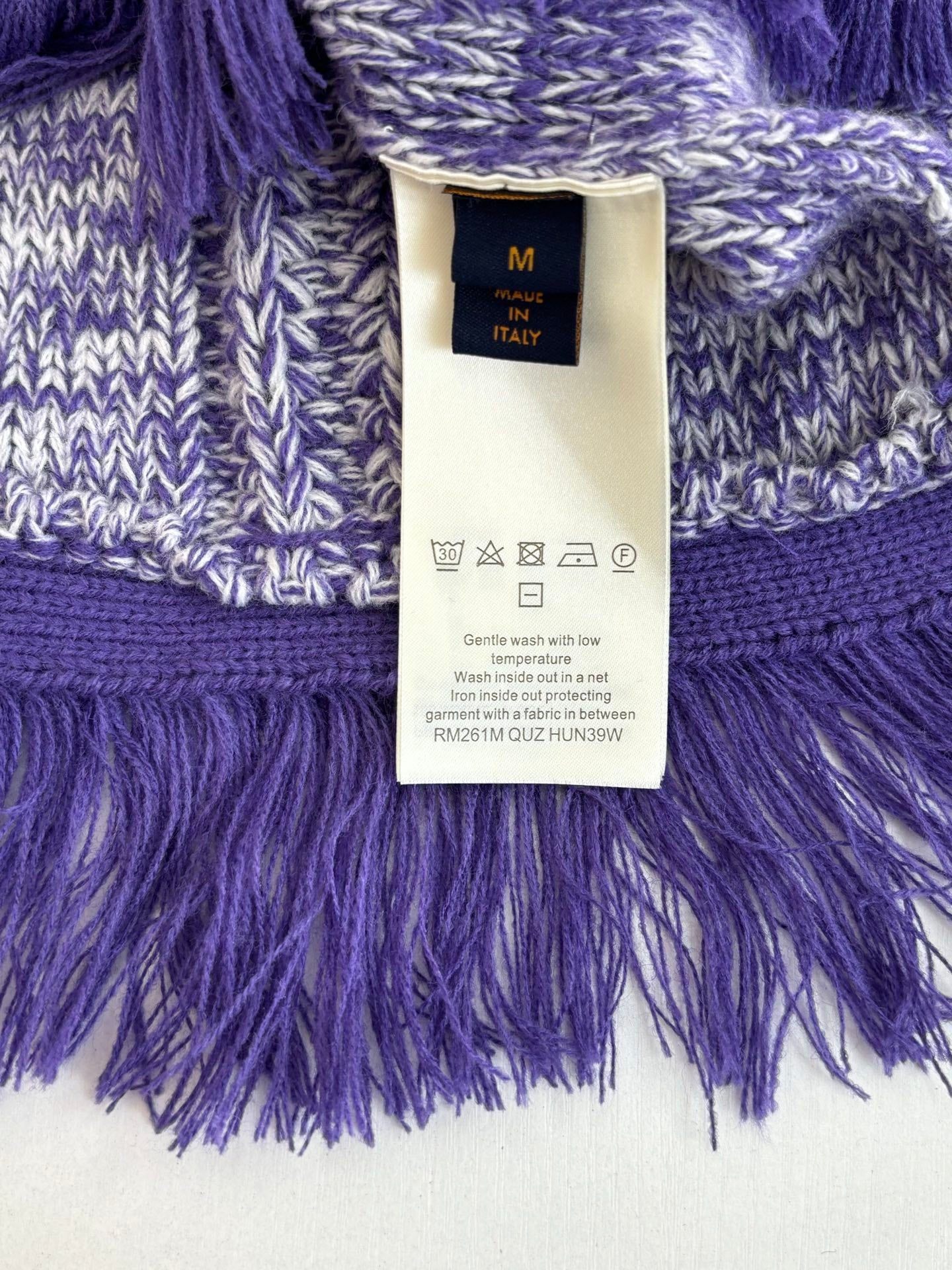 Knit sweater label area with size tag, heathered blue fabric and purple fringe hem