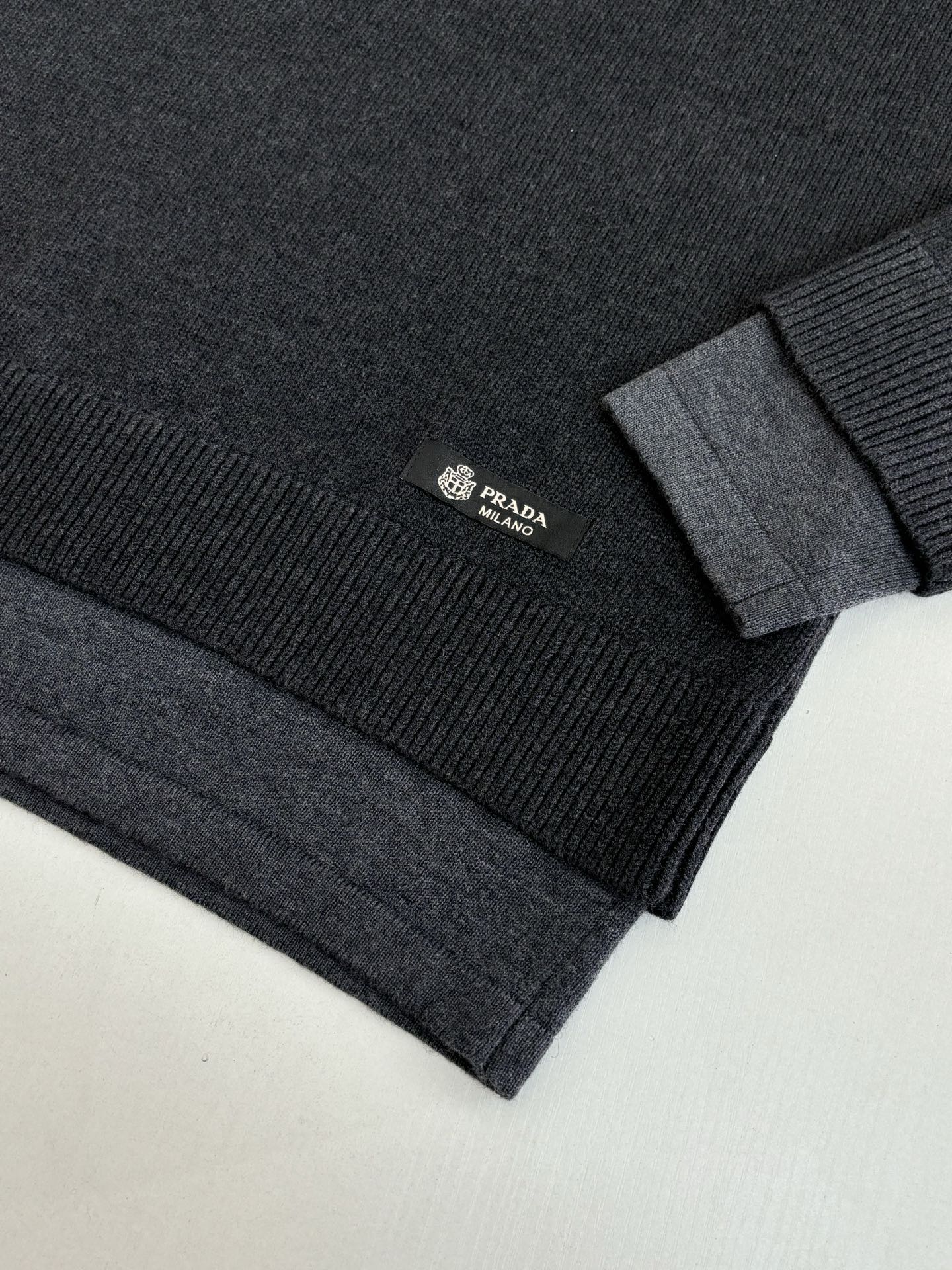 Dark knit sweater sleeve and hem detail with Prada logo patch