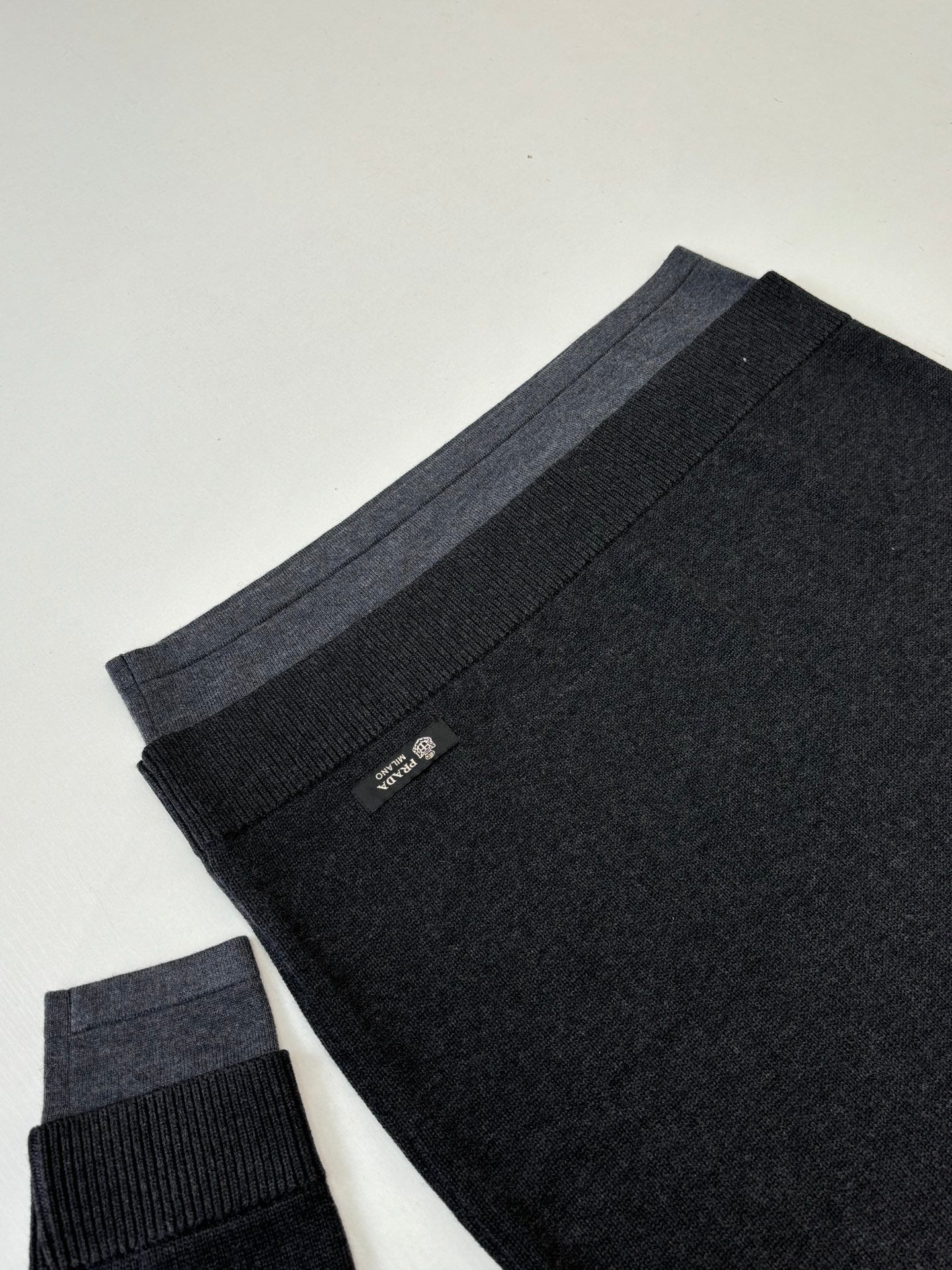 Dark knit sweater folded view with ribbed hem and small Prada tag