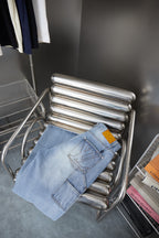 Light blue denim pants on a chrome display rack with patch pockets