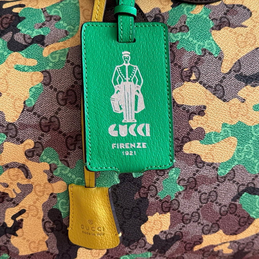 Green Gucci Firenze luggage tag on camo bag with yellow key charm