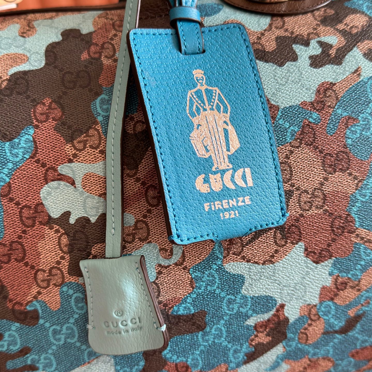 Duﬀel bag close-up of blue leather luggage tag and small white logo tag