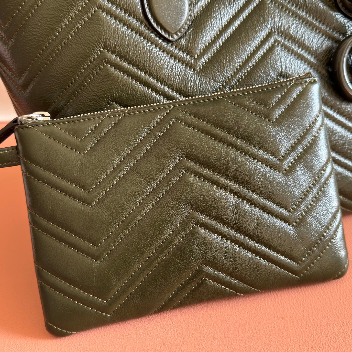 Olive green quilted leather zip pouch with chevron stitching and strap