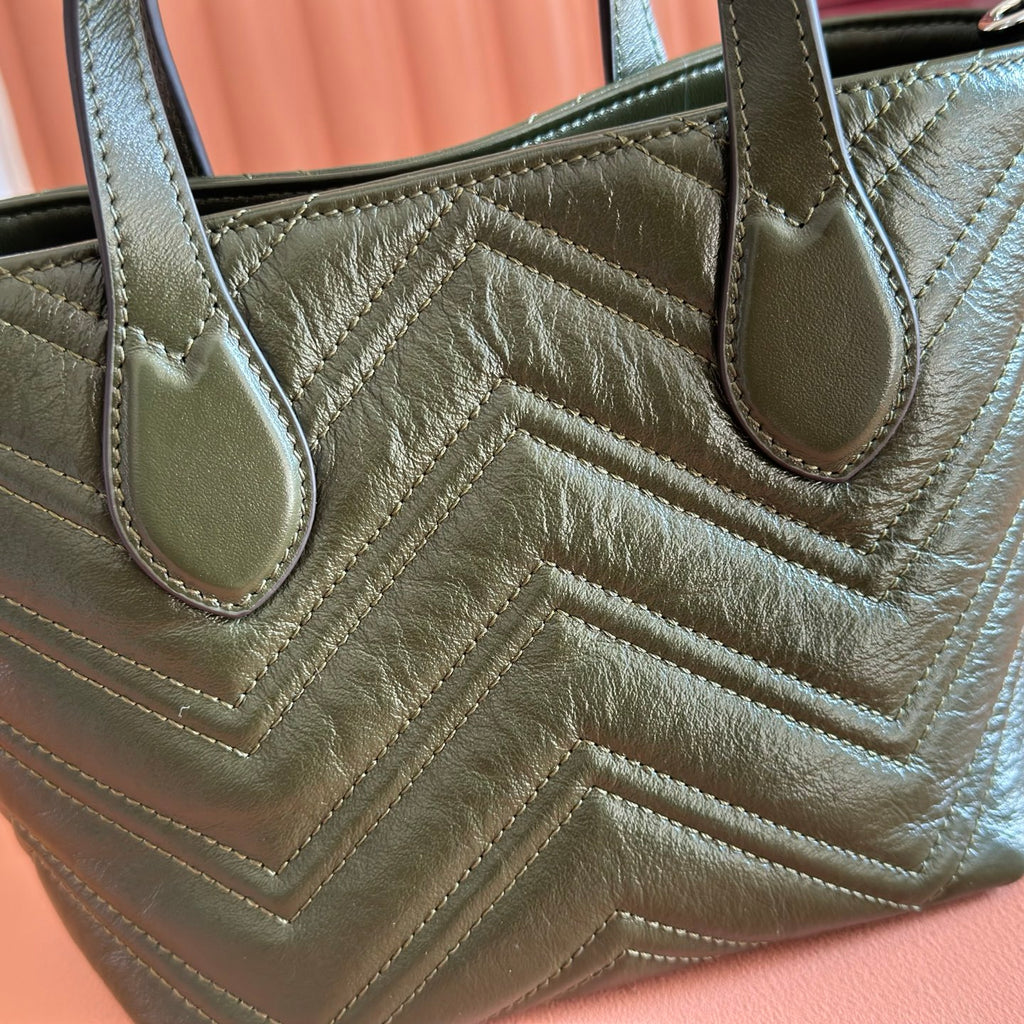 Close-up of dark green quilted leather handbag with curved handles and stitched chevron pattern