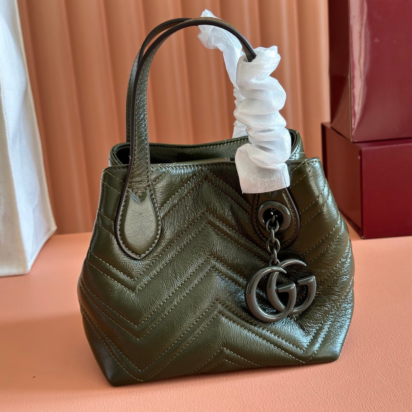 Dark green quilted leather handbag with top handle, white fabric tie, and double-G charm