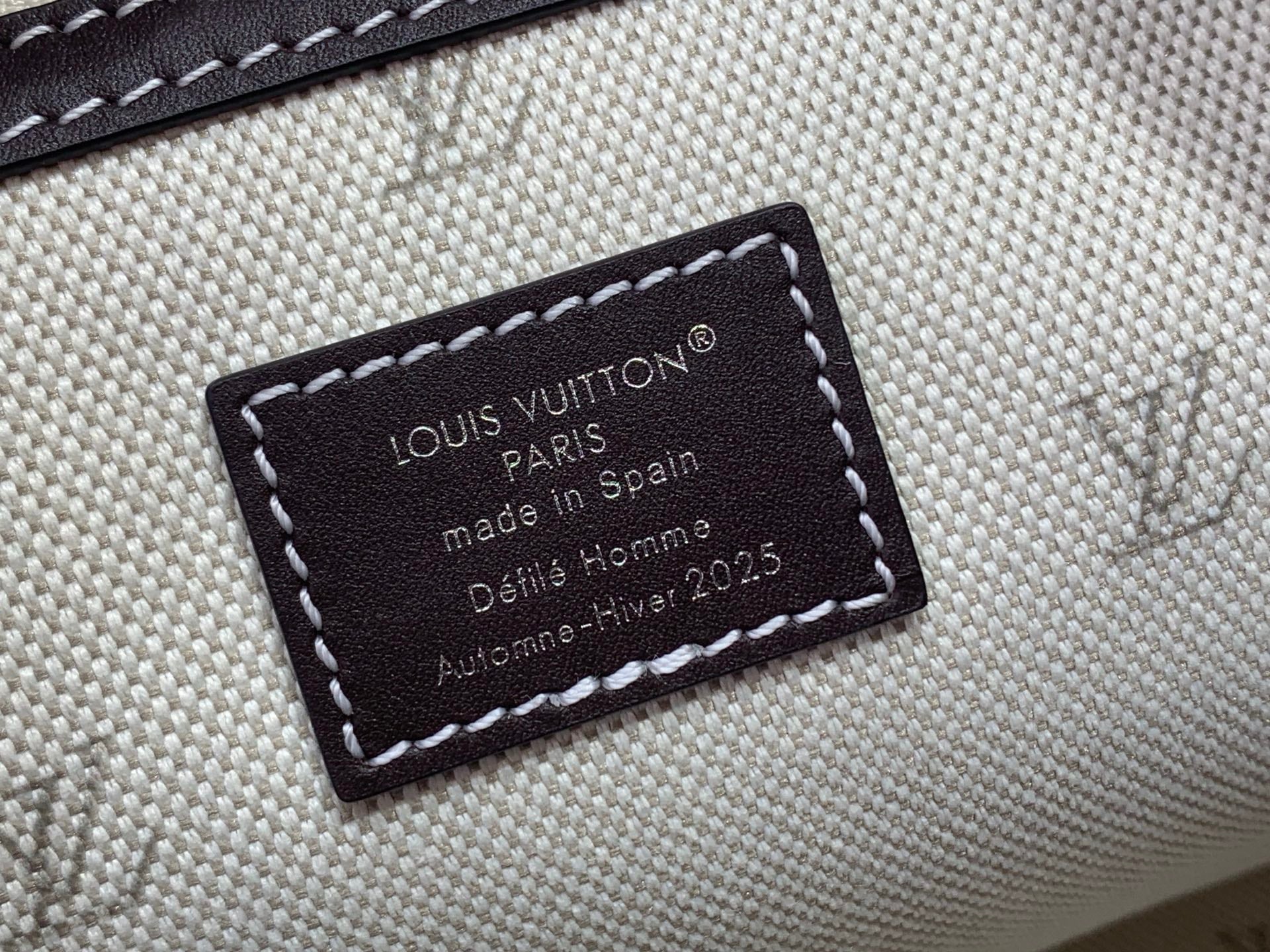 Louis Vuitton interior label on light canvas, dark stitched tag with made in Spain text.