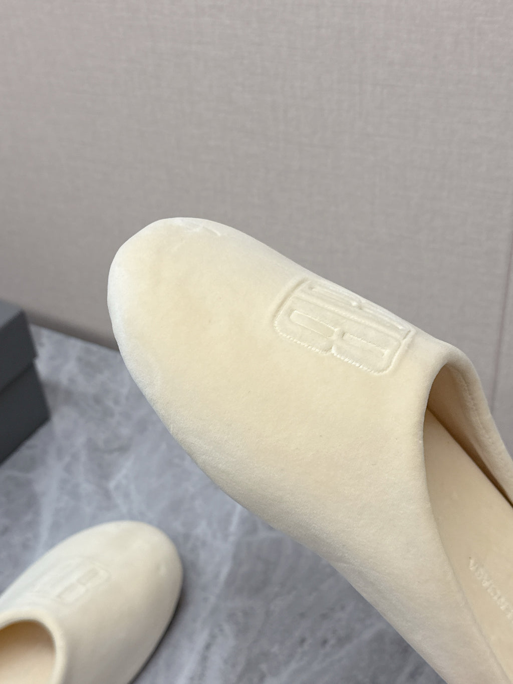 Balenciaga cream slide sandal angled close-up, embossed logo on outer upper
