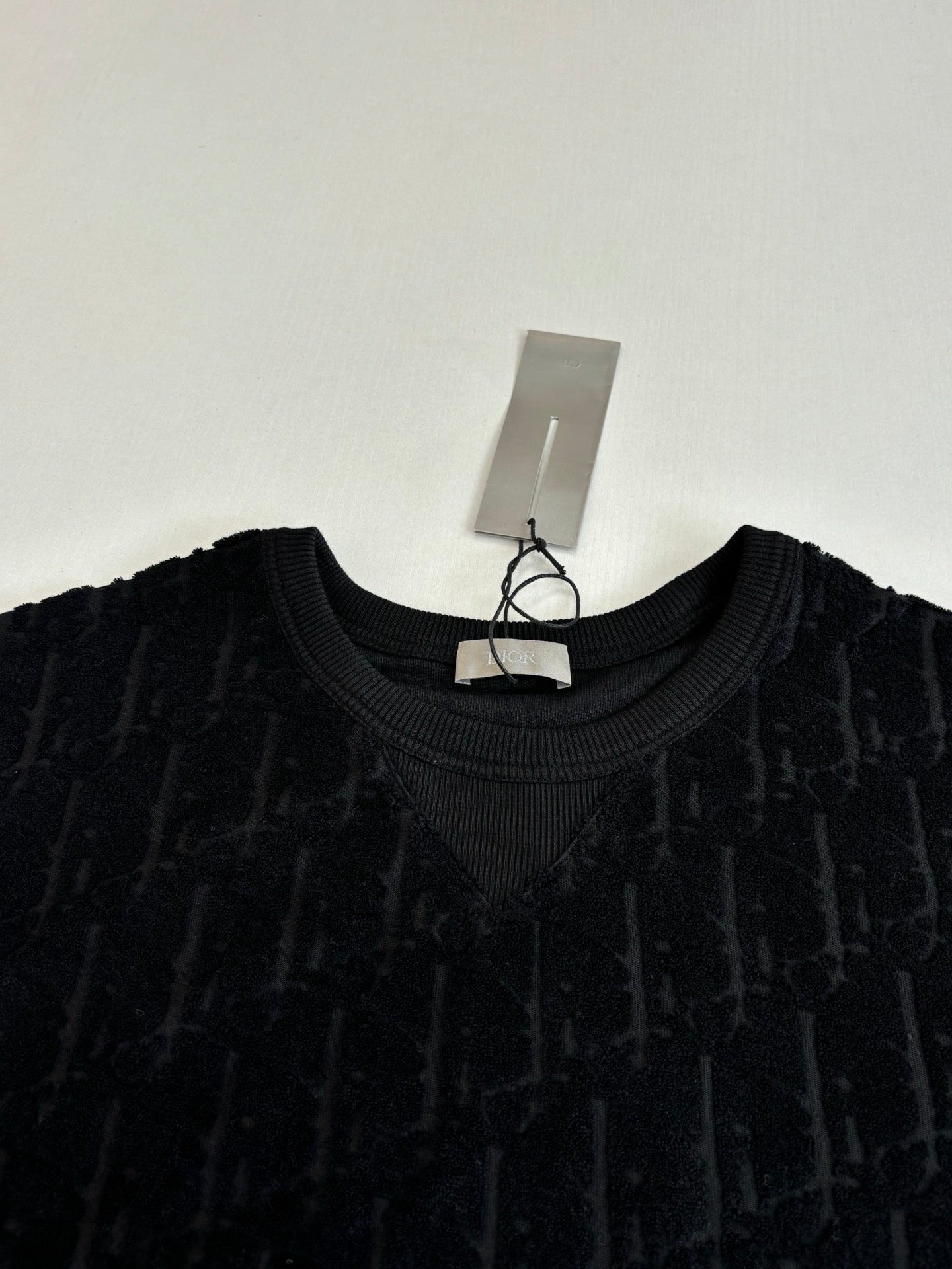 Crew-neck knit top, dark with allover logo texture; close view of neckline