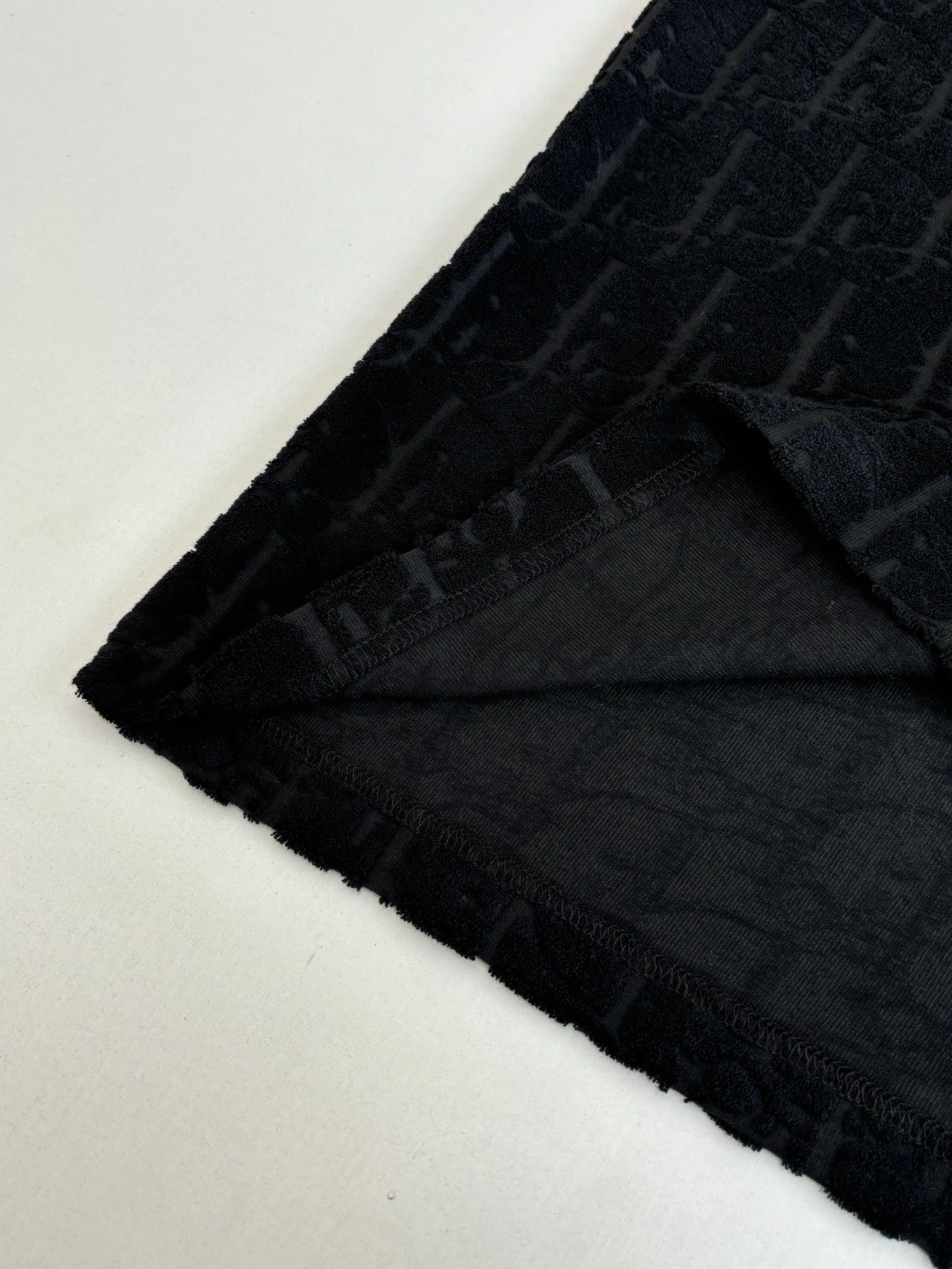 Hem and side view of dark textured knit, with logo pattern and curved bottom