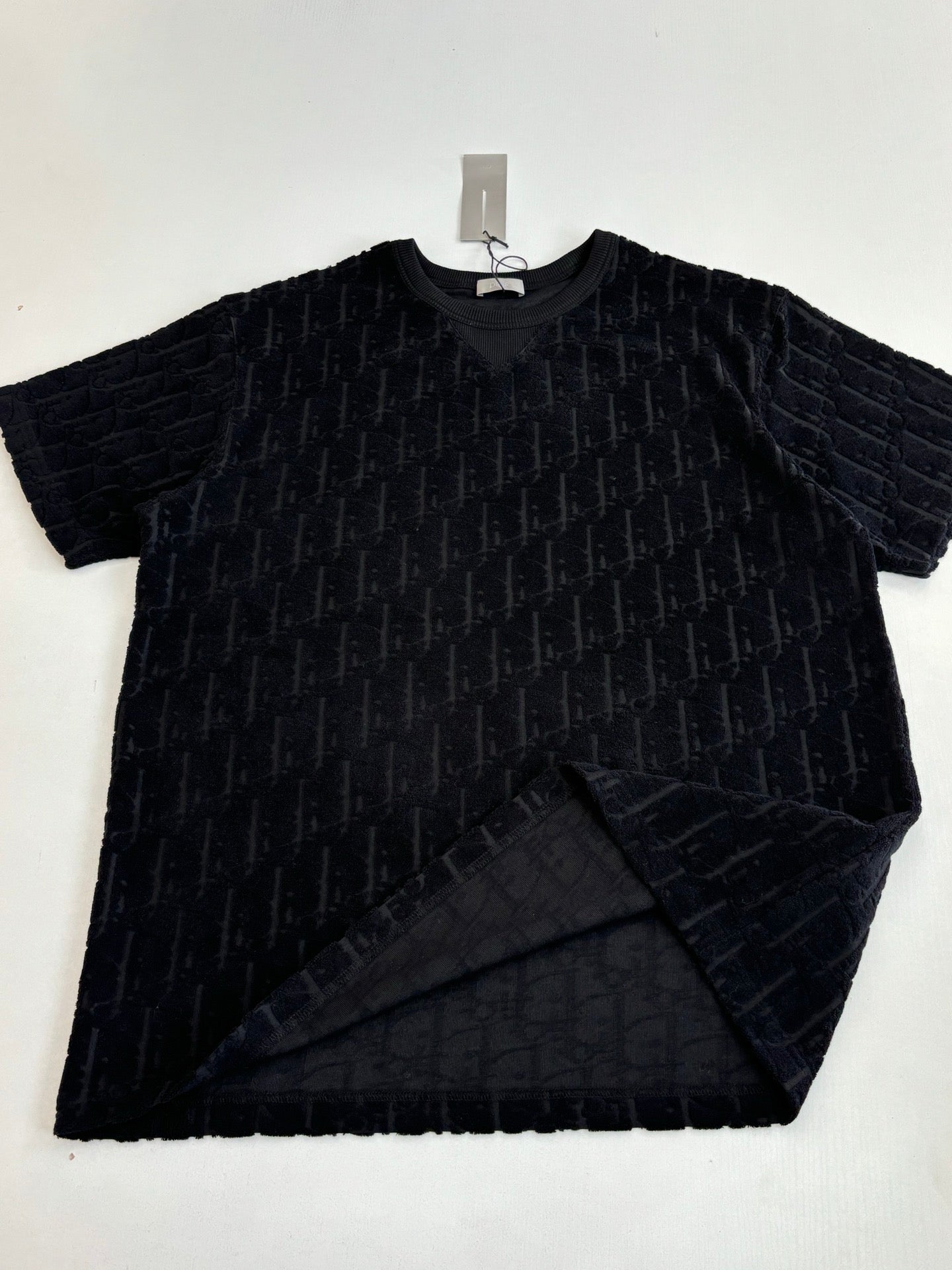 Short-sleeve knit top laid flat, dark textured fabric with logo pattern