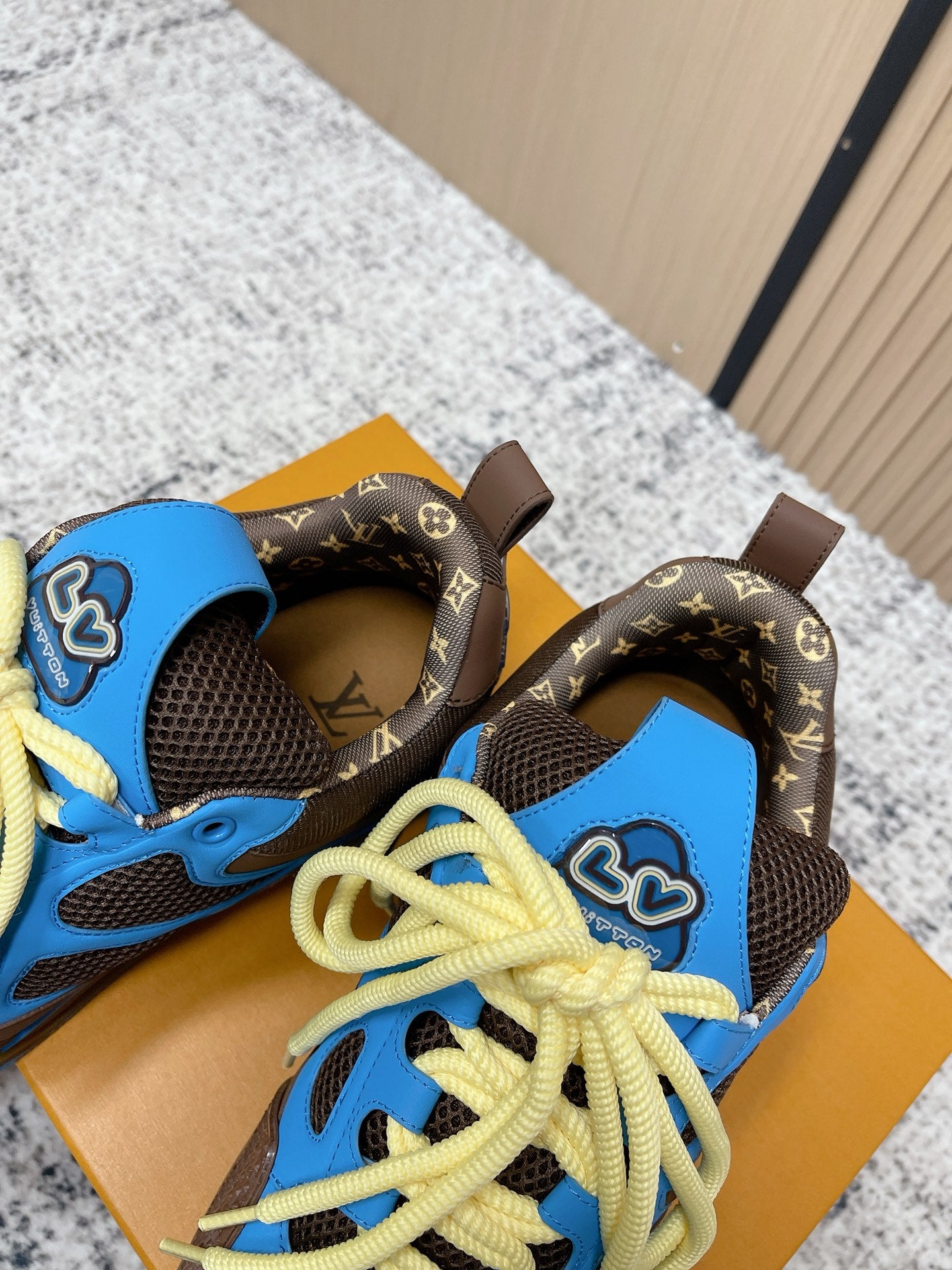 Unisex sneakers close-up: blue tongue, dark brown patterned panels, neon yellow laces