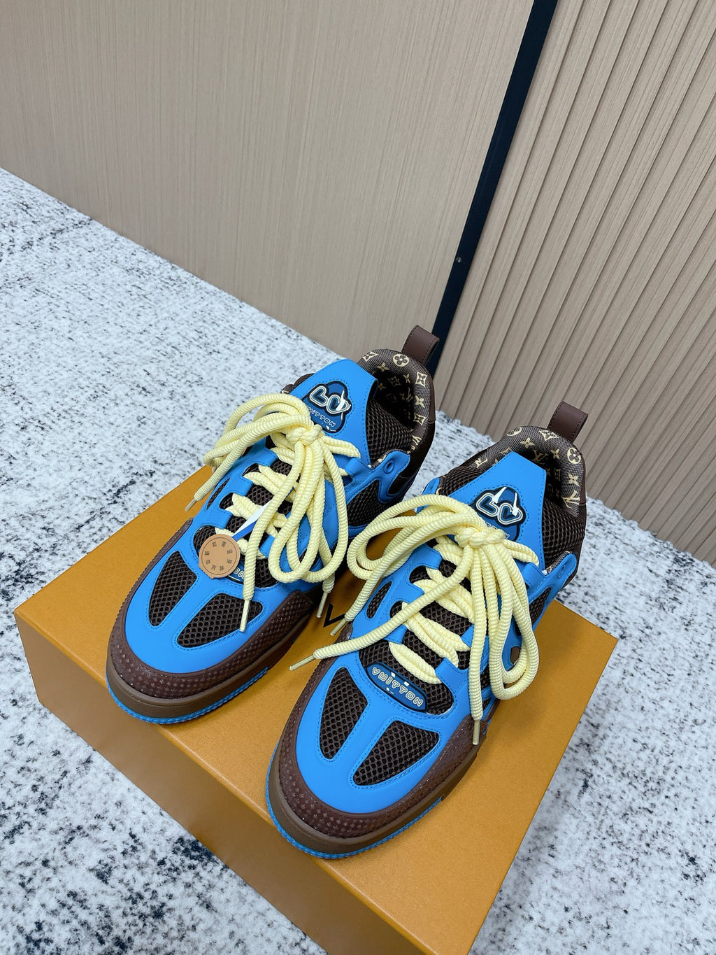 Unisex sneakers in blue and dark brown with neon yellow laces, on a shoebox