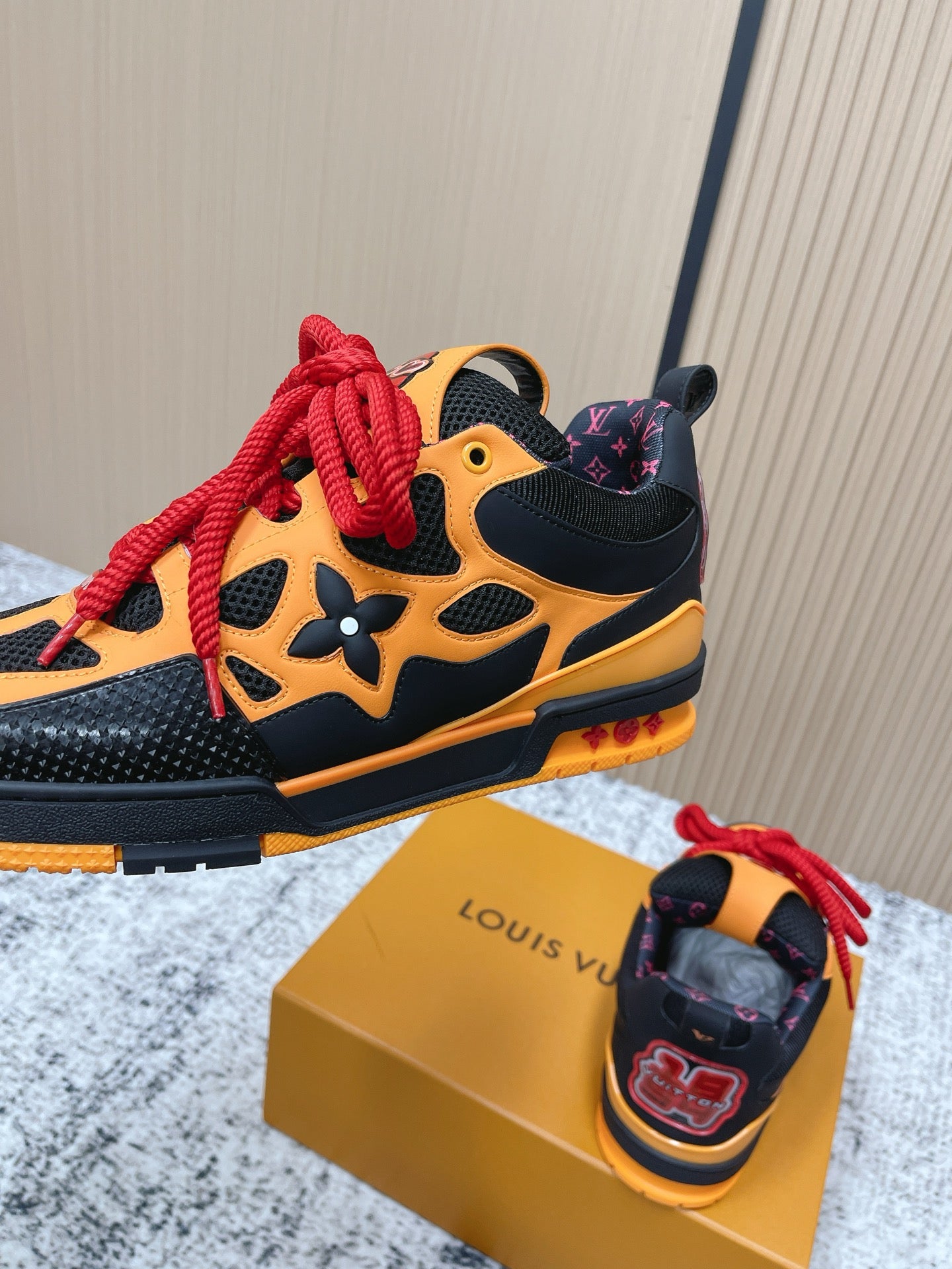 Black and orange sneakers with red laces, shown beside gold box for a side view.
