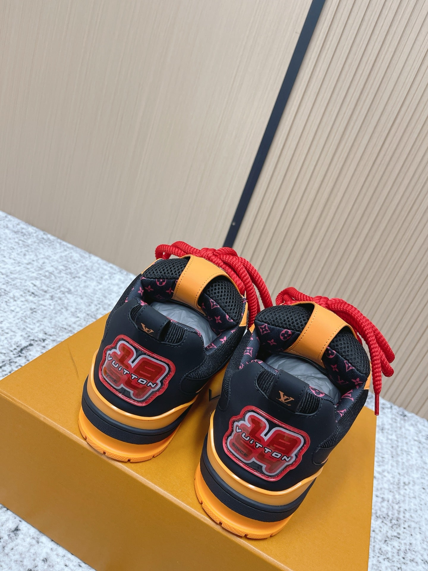 Black low-top sneakers on gold box with red laces, orange trim, and heel strap.