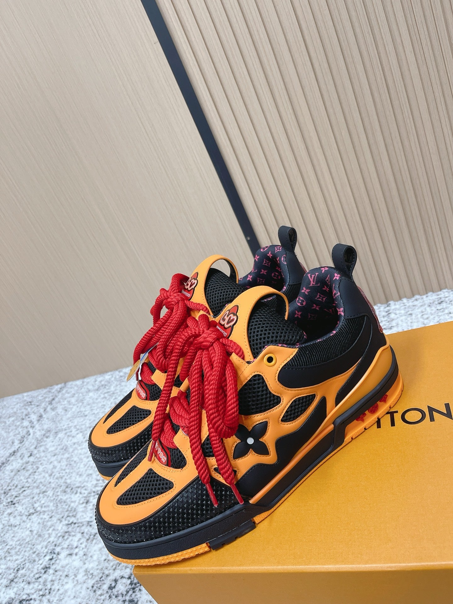 Black and orange sneakers with red laces, shown front angle on a gold box.