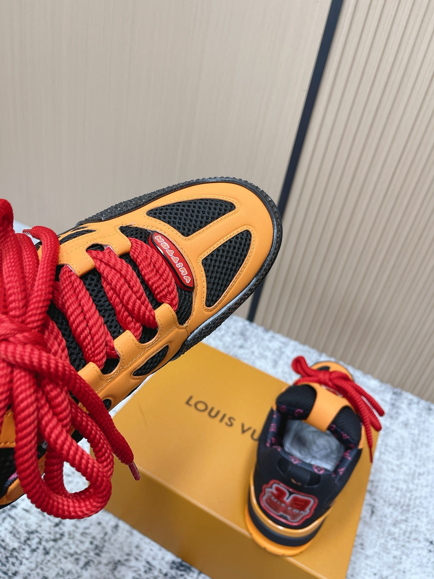 Orange and black sneaker side view with red laces and textured sole on box.