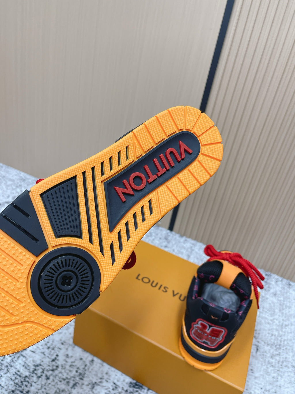 Sneaker outsole in orange and black with tread, plus matching pair on gold box.
