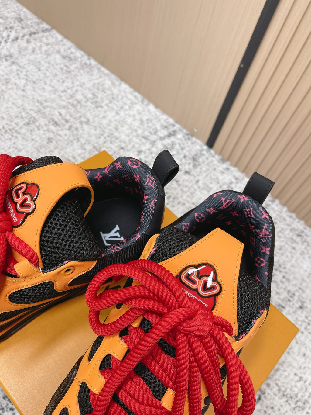 Black sneakers with orange side panels, red laces, and patterned interior heel detail.