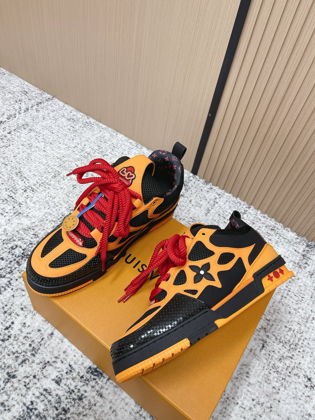 Black and orange lace-up sneakers on gold box, red laces and multicolor accents.