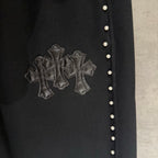 Black pants with embroidered cross emblem and a row of small side buttons