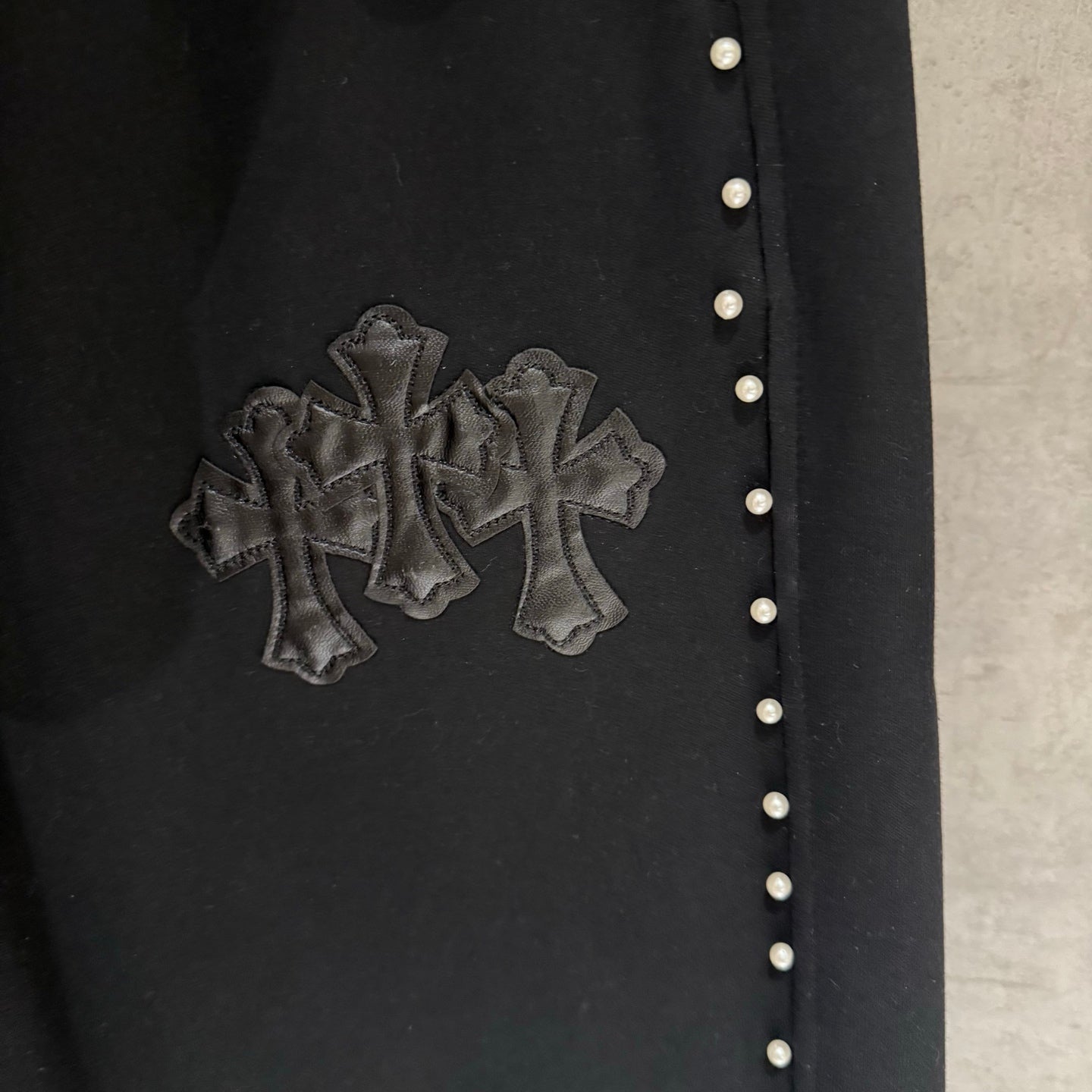 Black pants with embroidered cross emblem and a row of small side buttons