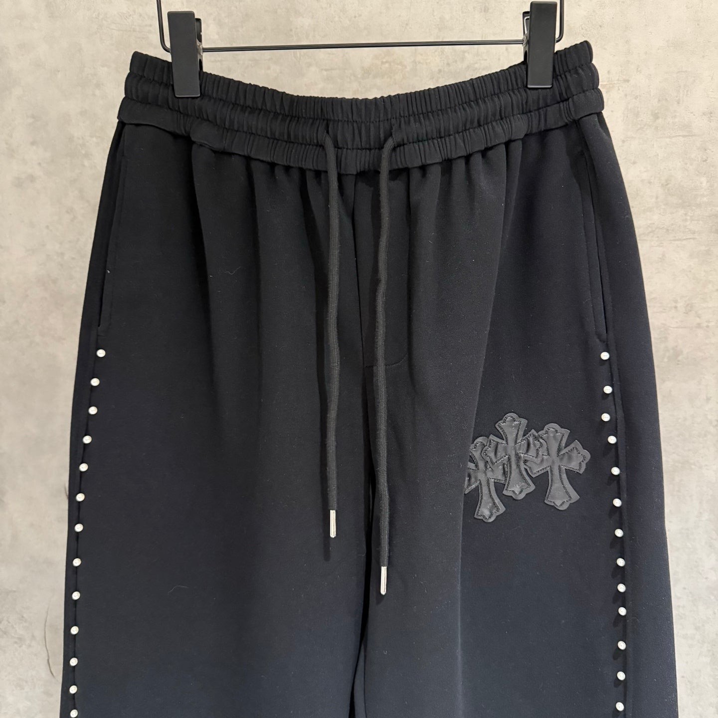 Black wide-leg pants, elastic waistband with drawstrings; side stud stripes and cross emblem