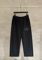 Black wide-leg pants with drawstring waist and side stud trim, embroidered cross patch