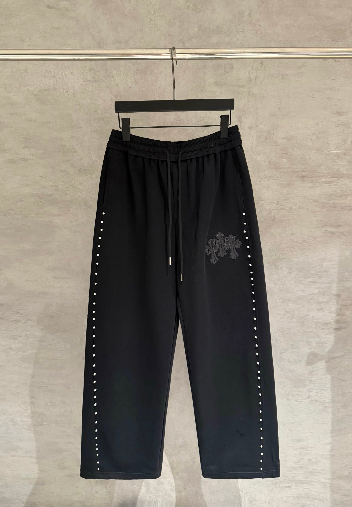Black wide-leg pants with drawstring waist and side stud trim, embroidered cross patch