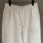 White cropped pants close-up of elastic waistband and decorative cross applique