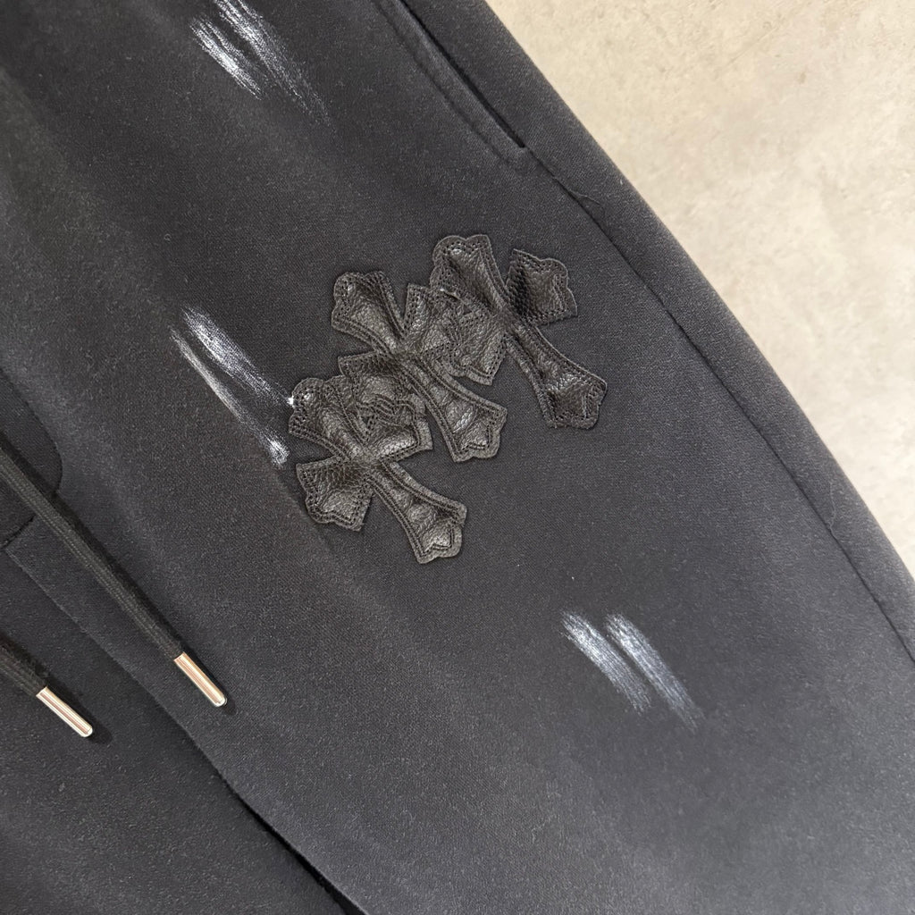 Black pants with cross-like embroidered patch and glossy reflective spots