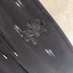 Black pants with cross-like embroidered patch and glossy reflective spots