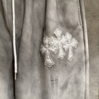 Chrome pants close-up with silver cross embroidery on light gray fabric