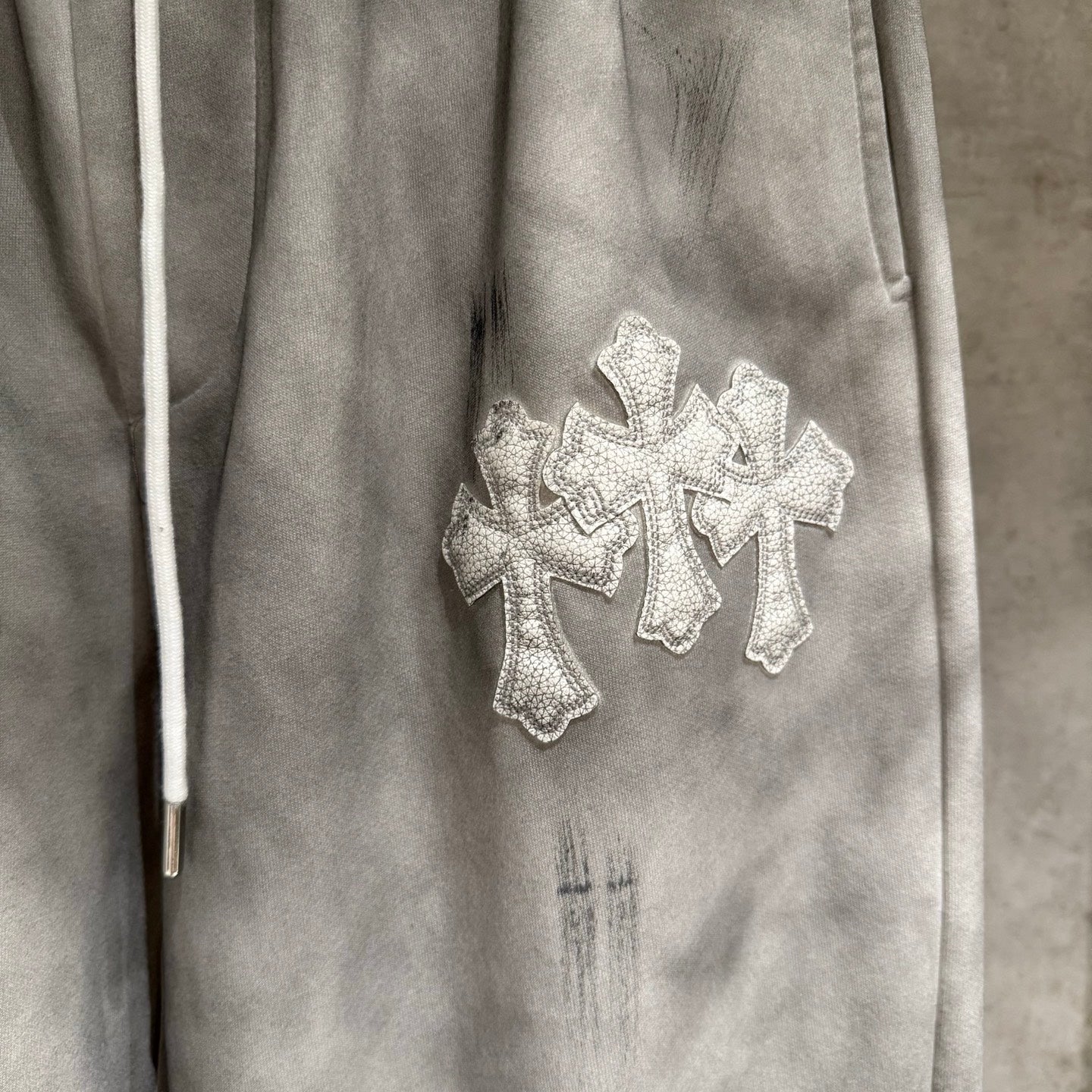Chrome pants close-up with silver cross embroidery on light gray fabric