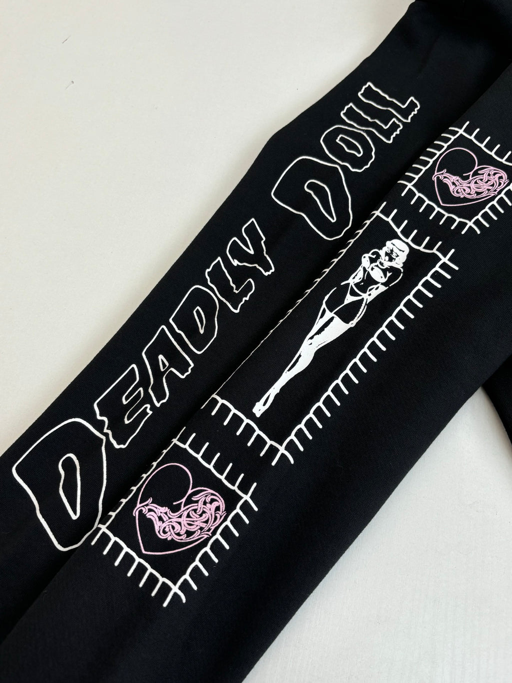 Black hoodie sleeve detail with white text, stitched-style graphics, and pink accents