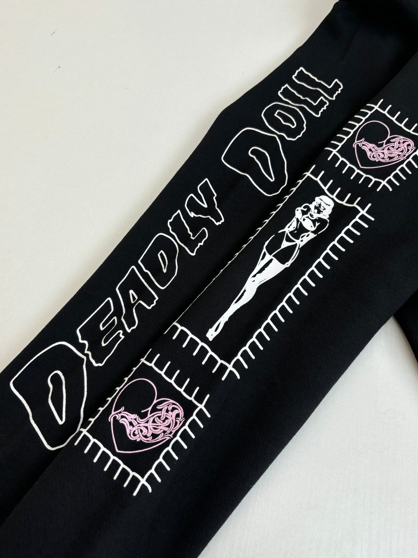 Black hoodie sleeve detail with white text, stitched-style graphics, and pink accents