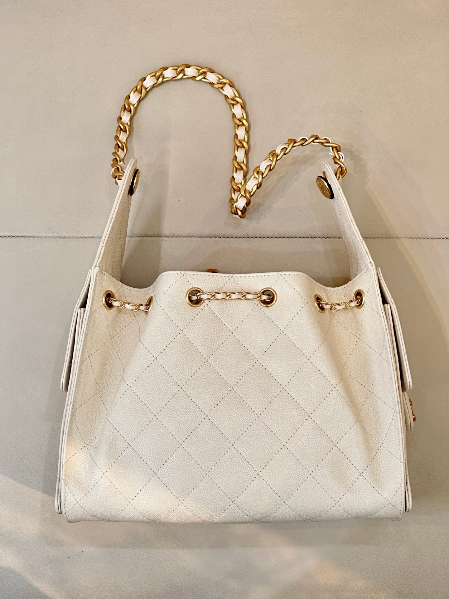 Chanel quilted white leather bucket bag with open top, gold chain strap, and CC logo detail