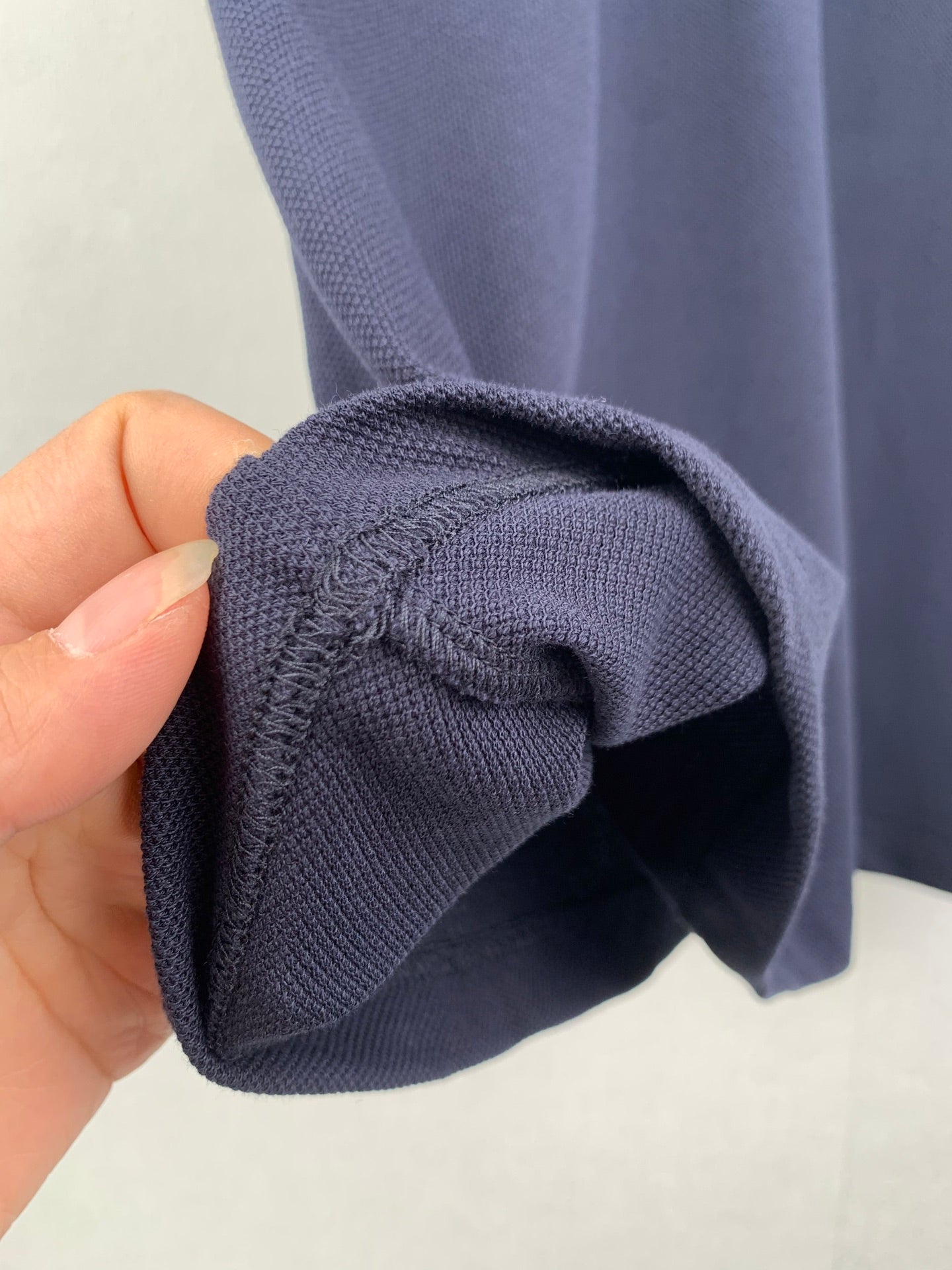 Navy polo shirt cuff and sleeve opening, knit texture shown by hand
