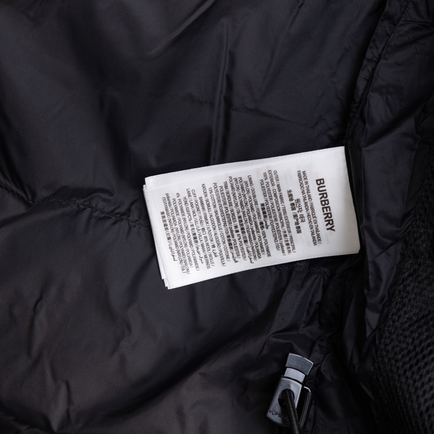 Long black puffer jacket showing Burberry fabric tag and zip pocket