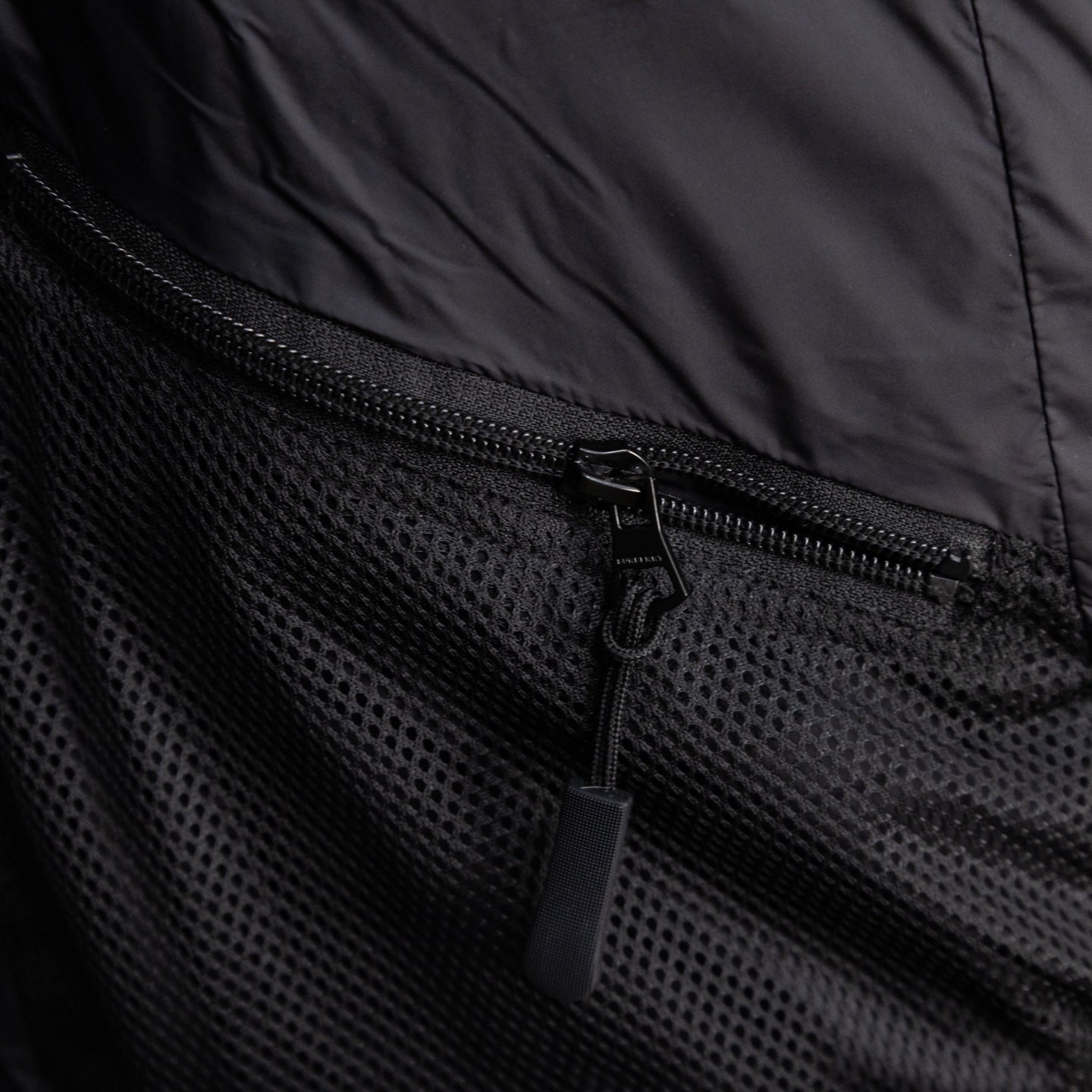 Black puffer vest pocket with mesh fabric and exposed zipper pull