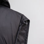 Black quilted puffer vest with hood, stitched shoulder panel, and visible cuff seam